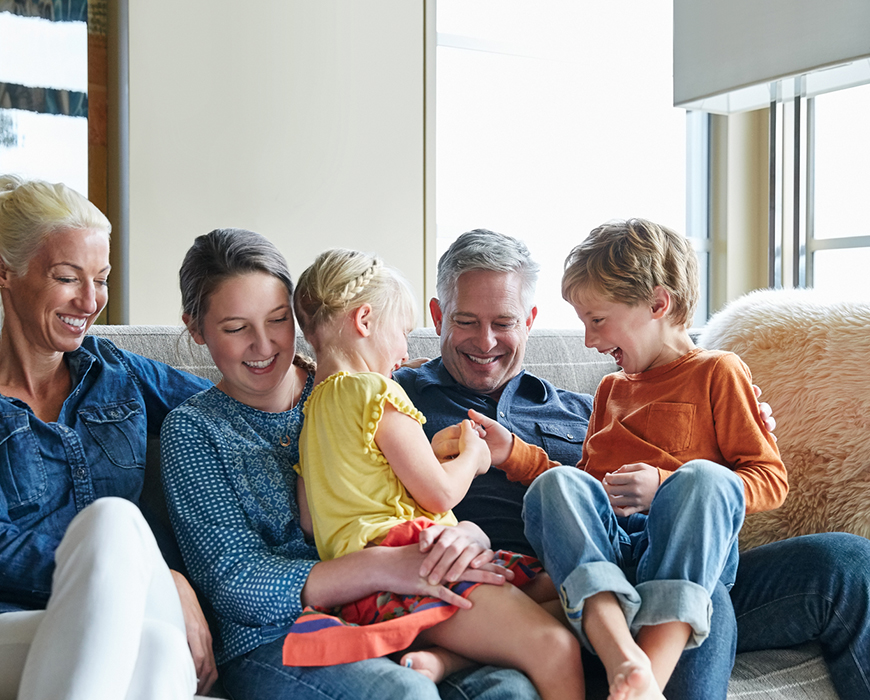 A family with two children laughing on the couch.