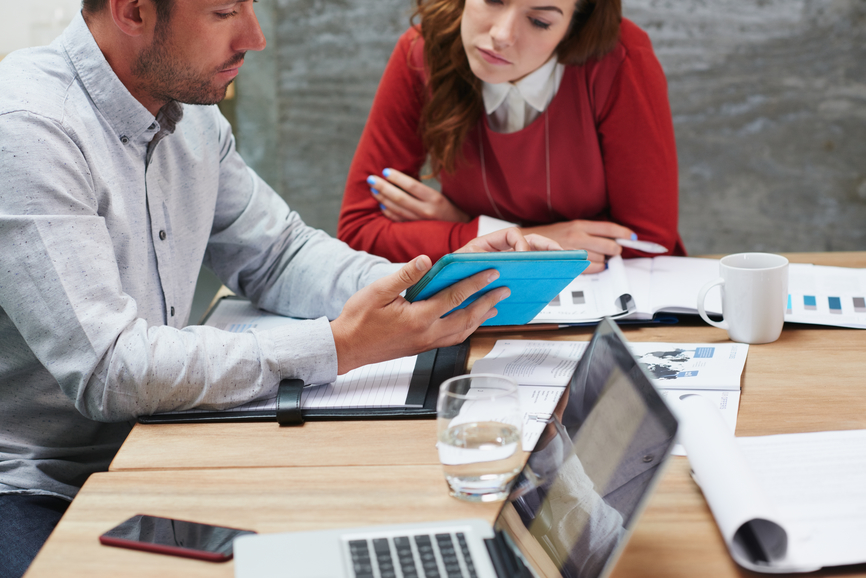 Business people engaging in team brainstorm workshop using smartdevice checking profit growth graphs printed documents in trendy office space