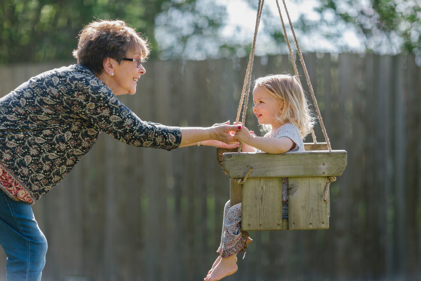 A grandma playing it a child in a swing.